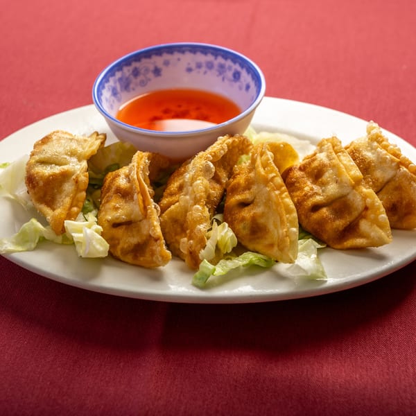 Golden-fried dumplings with lettuce and a side of sweet chili sauce on a white plate.