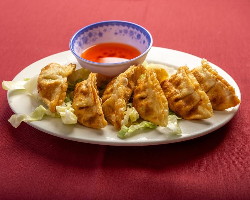 Golden-fried dumplings with lettuce and a side of sweet chili sauce on a white plate.