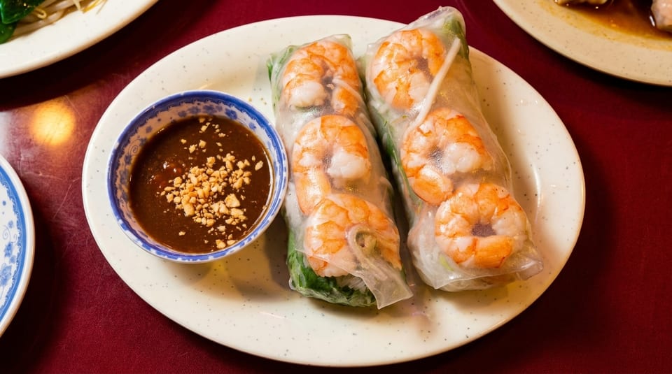 Two fresh spring rolls with shrimp and greens, served with a side of peanut sauce.