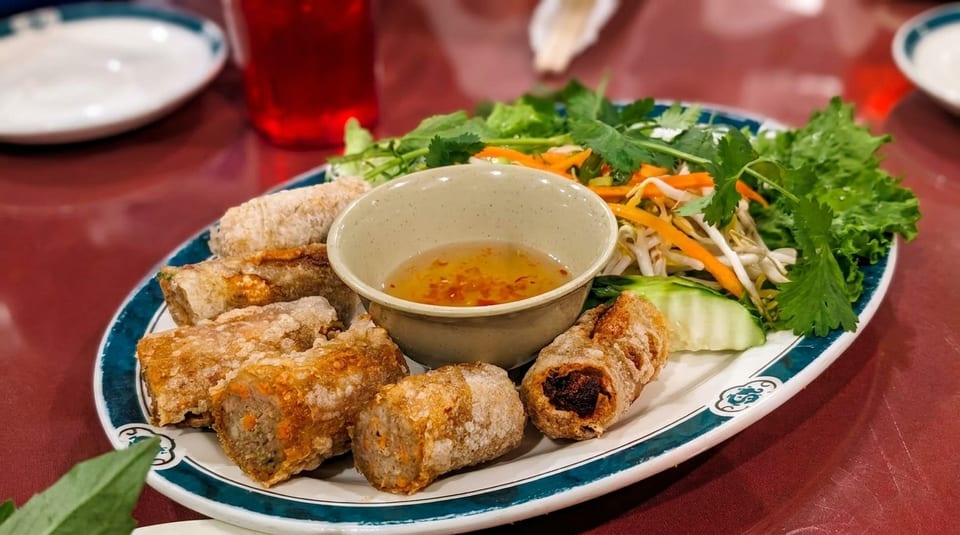Crispy fried spring rolls, fresh lettuce, bean sprouts, carrots, cucumber, and dipping sauce on a plate.