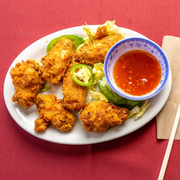 Crispy fried chicken wings with jalapeños, lettuce, and sweet chili sauce on a white plate.